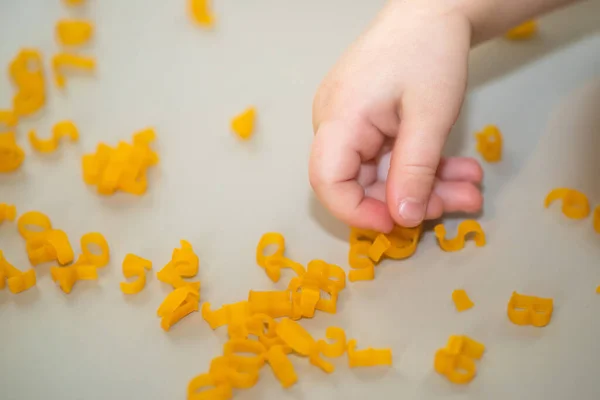 hand of child collecting letters from pasta from table. development of fine motor skills of hands. Montessori technique. Learn letters and alphabet in game.