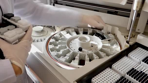 实验室里的女孩把血清样本放在医疗设备里进行分析 机器自动生化分析 相机是固定的 — 图库视频影像