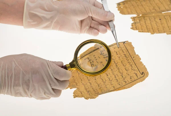 A researcher studies Arabic writing from the Koran using a magnifying glass and a table with a light. Paleography, the study of ancient Arabic writing