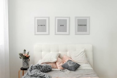 Işık bahar yatak odası iç çiçek ve çerçeve gri yatağın yanında. Gün ışığı alan minimalist Oda Dekorasyon.