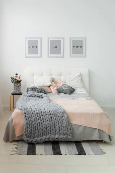 Light spring bedroom interior with flowers and frames near the grey bed. Minimalist room decor with daylight