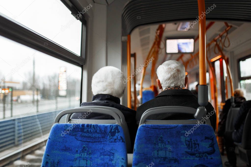 Senior couple travelling on the bus. There are other people sat on the bus who are in the background.