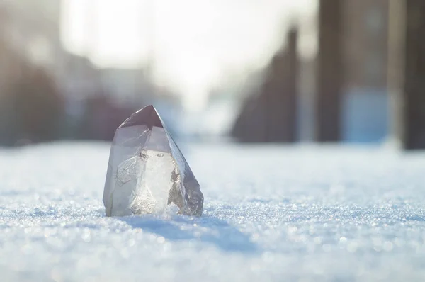 Snow-white crystal of pure transparent quartz on snow. Chalcedony contrast on background of blurred city lines Stock Photo