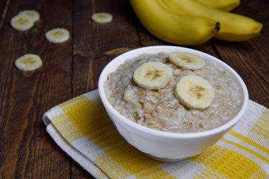muz dilimleri ile sıcak bir ahşap arka plan üzerinde güzel bir beyaz kase yulaf ezmesi