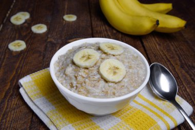 muz dilimleri ile sıcak bir ahşap arka plan üzerinde güzel bir beyaz kase yulaf ezmesi