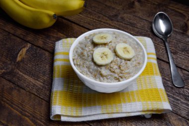 muz dilimleri ile sıcak bir ahşap arka plan üzerinde güzel bir beyaz kase yulaf ezmesi