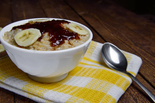 Aveia em uma bela tigela branca em um fundo de madeira quente com fatias de bananas e geléia — Fotografia de Stock