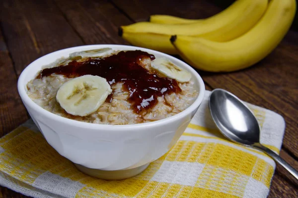 Harina de avena en un hermoso tazón blanco sobre un fondo de madera caliente con rodajas de plátanos y mermelada —  Fotos de Stock