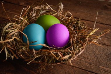 ahşap arka plan üzerinde bir hasır saman yuvadaki boyalı Paskalya yumurtaları