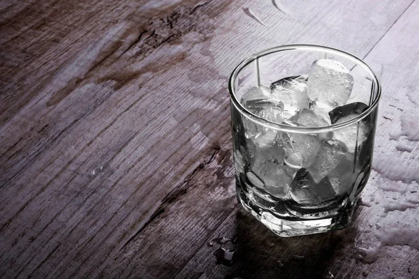 Glass with ice on a wooden background — Stock Photo, Image