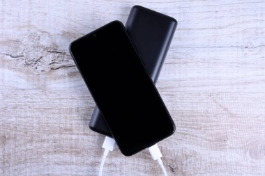 Telefon şarjı, elektrik faturası akıllı telefon, enerji bankasıyla cep telefonu. Tahta arkaplanda Güç Bankası alanının derinliği