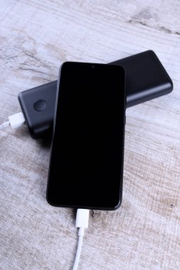 Telefon şarjı, elektrik faturası akıllı telefon, enerji bankasıyla cep telefonu. Tahta arkaplanda Güç Bankası alanının derinliği