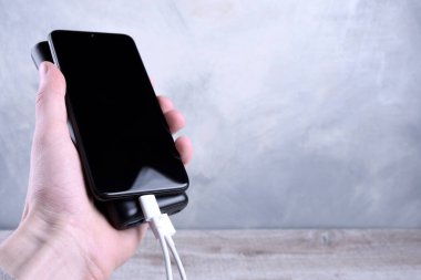 Telefon şarjı, elektrik faturası akıllı telefon, enerji bankasıyla cep telefonu. Güç bankacılarının derinliği ahşap arka planda el ele tutuşuyor.