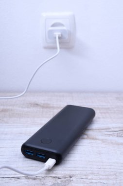 Siyah telefon güç bankası ahşap arka planda şarj olmak için prize takılmış.
