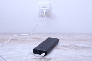 Siyah telefon güç bankası ahşap arka planda şarj olmak için prize takılmış.