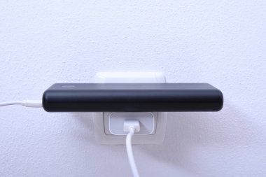 Siyah telefon güç bankası ahşap arka planda şarj olmak için prize takılmış.