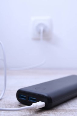 Siyah telefon güç bankası ahşap arka planda şarj olmak için prize takılmış.