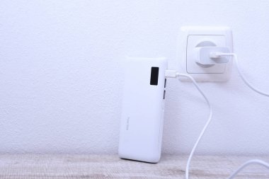 Siyah telefon güç bankası ahşap arka planda şarj olmak için prize takılmış.