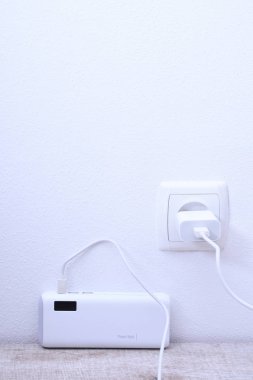 Siyah telefon güç bankası ahşap arka planda şarj olmak için prize takılmış.