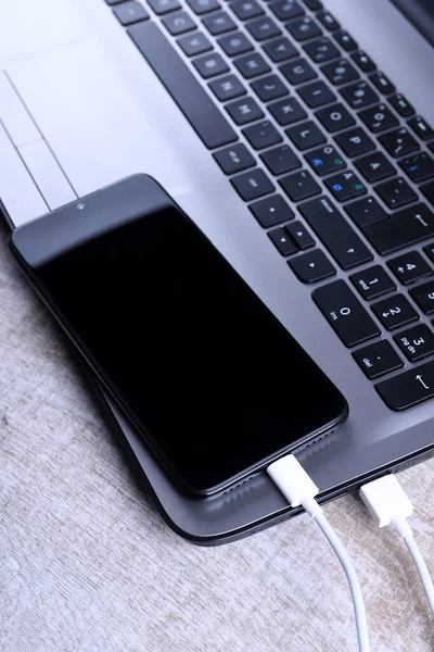 Branchez le cordon USB, le chargeur de câble, la charge, le chargement et le transfert de données du téléphone portable, smartphone avec un ordinateur portable sur le sol en bois, vue sur la table — Photo