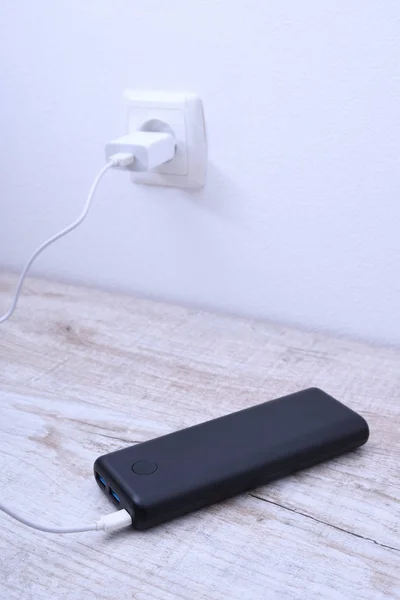 Чорний телефон, підключений до гнізда на стіні для зарядки на дерев'яному фоні — стокове фото