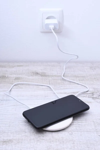 Мобільний телефонний заряд на бездротовому зарядному пристрої, концепція сучасного обладнання на дерев'яному фоні столу — стокове фото