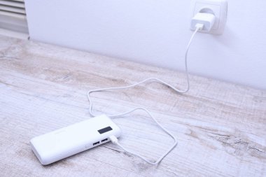Beyaz telefon güç bankası ahşap arka planda şarj olmak için prize takılmış.