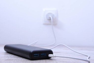 Siyah telefon güç bankası ahşap arka planda şarj olmak için prize takılmış.