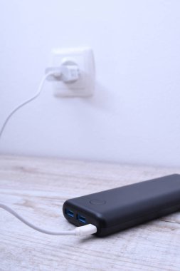Siyah telefon güç bankası ahşap arka planda şarj olmak için prize takılmış.