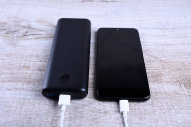 Telefon şarjı, elektrik faturası akıllı telefon, enerji bankasıyla cep telefonu. Tahta arkaplanda Güç Bankası alanının derinliği