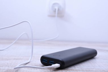 Siyah telefon güç bankası ahşap arka planda şarj olmak için prize takılmış.