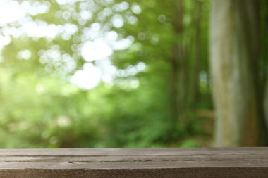 Yeşil yaprakların ve ağaçların bulanık arkaplanının önündeki gri ahşap masa resmi