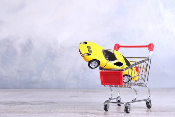 Concept of buying a new car. Toy car in shopping basket on wooden background — 스톡 사진