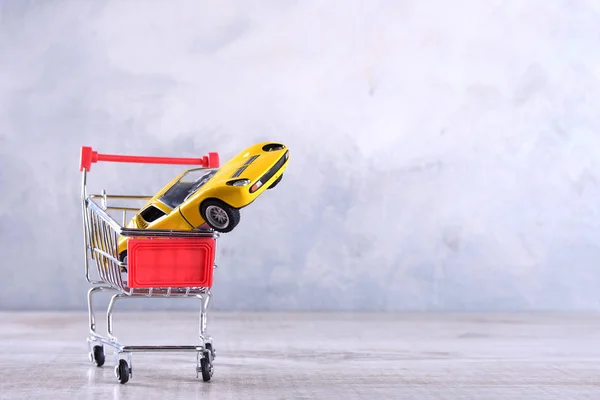 Begreppet köpa en ny bil. Leksaksbil i kundvagn på trä bakgrund — Stockfoto