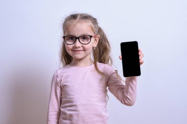 Küçük beyaz bir kızın portresi gri arka plandaki telefonu işaret ediyor.