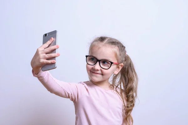Retrato de uma menina branca fazer selfie em um telefone celular em um fundo cinza — Fotografia de Stock