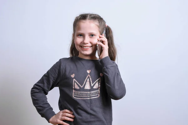 Retrato de uma menina branca fala por telefone em um fundo cinza — Fotografia de Stock