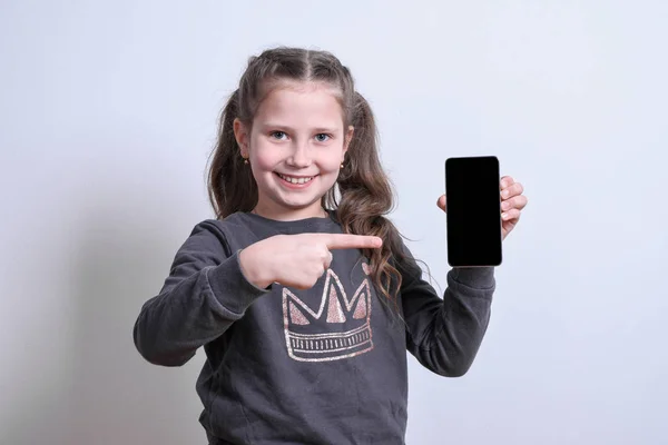 Retrato de uma menina branca aponta para o telefone em um fundo cinza — Fotografia de Stock