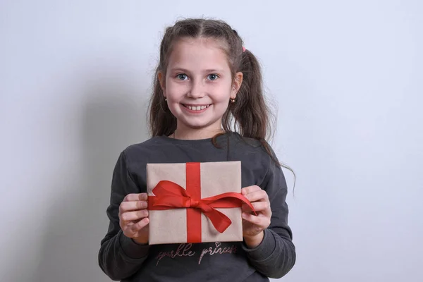 Retrato de uma menina branca mostra estende o presente em um fundo cinza — Fotografia de Stock