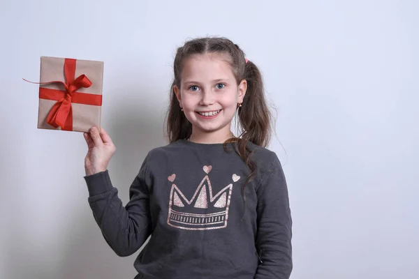 Retrato de uma menina branca mostra estende o presente em um fundo cinza — Fotografia de Stock