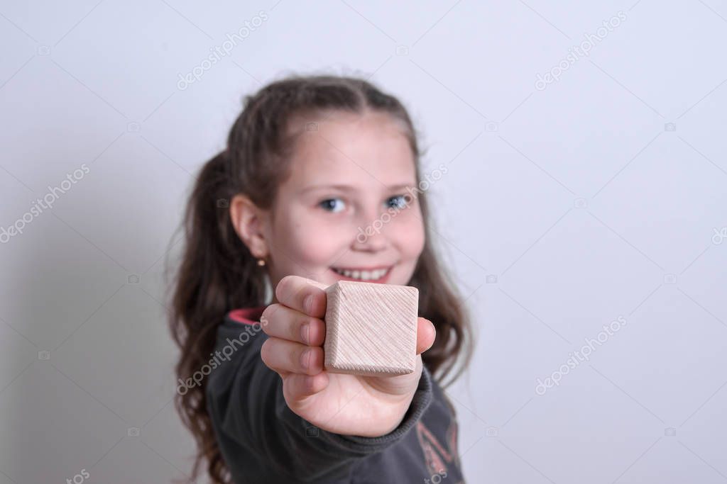 Portrait of a little white girl holding a blank wooden cube on a gray background