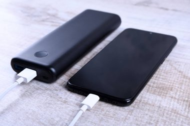 Telefon şarjı, elektrik faturası akıllı telefon, enerji bankasıyla cep telefonu. Tahta arkaplanda Güç Bankası alanının derinliği