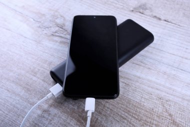 Telefon şarjı, elektrik faturası akıllı telefon, enerji bankasıyla cep telefonu. Tahta arkaplanda Güç Bankası alanının derinliği