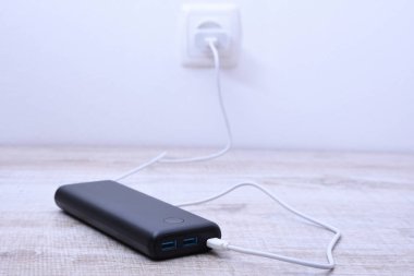 Siyah telefon güç bankası ahşap arka planda şarj olmak için prize takılmış.