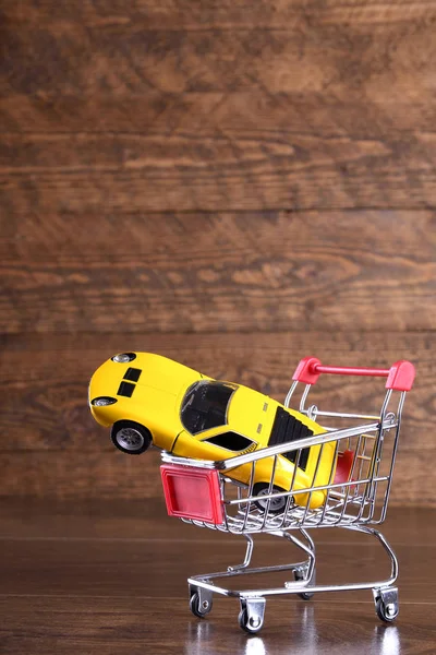 Begreppet köpa en ny bil. Leksaksbil i kundvagn på trä bakgrund — Stockfoto