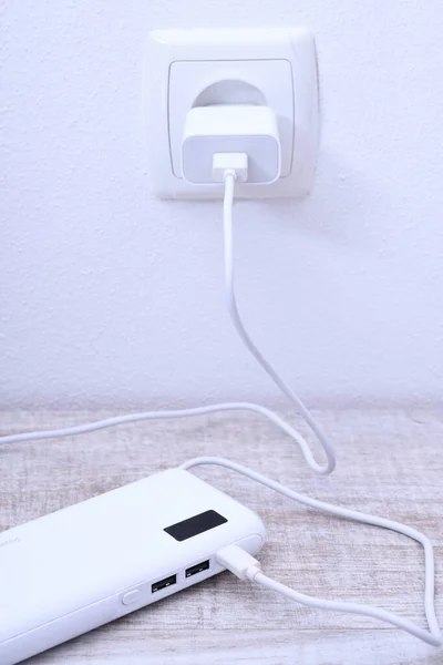 Banco de alimentación del teléfono blanco enchufado en el zócalo en la pared para cargar sobre fondo de madera — Foto de Stock