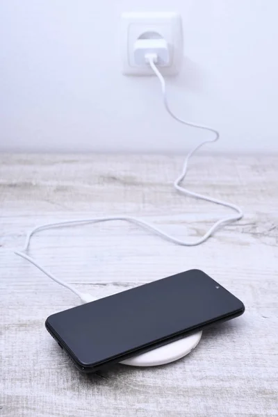 Мобільний телефонний заряд на бездротовому зарядному пристрої, концепція сучасного обладнання на дерев'яному фоні столу — стокове фото