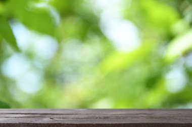 Yeşil yaprakların ve ağaçların bulanık arkaplanının önündeki gri ahşap masa resmi.