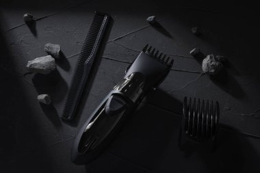 Üst Manzara. Koyu betonda saç ve kafa kesme makinesi, sert gölgeli taş arka plan.