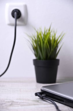 Laptop, bilgisayar duvarın yanındaki bir masada 220 voltluk bir prizden şarj oluyor. Enerji, birikim